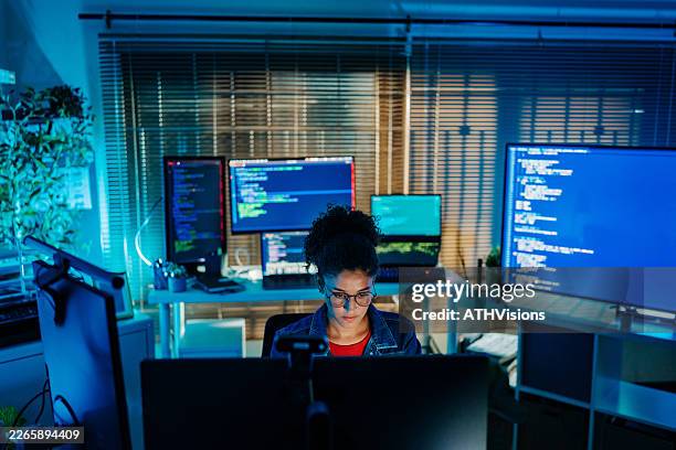 young latina software developer coding at multi-monitor workstation at night - multiple screens stock pictures, royalty-free photos & images