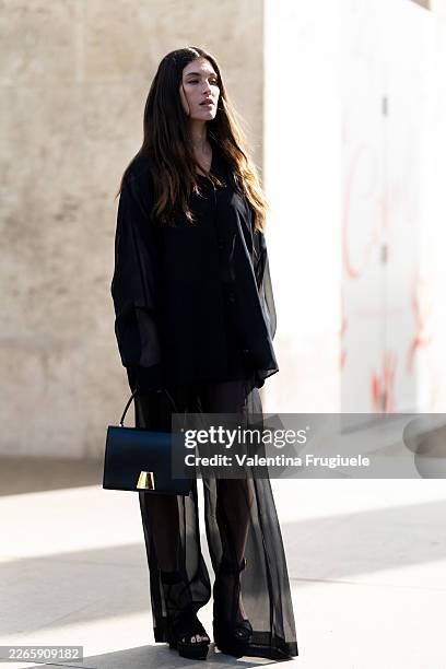 Rainey Qualley wears black heels, a black organza shirt, a black leather bag and black organza trousers outside Akris show during Day Seven of Paris...