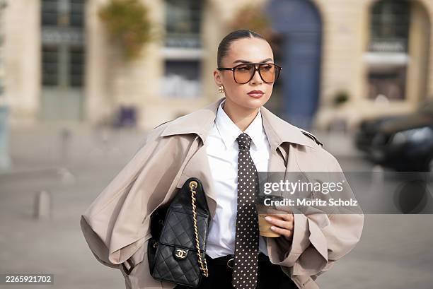 Anna Wein is seen wearing a beige oversized longline trench coat with wide lapels, exaggerated voluminous sleeves, epaulettes, straps on the sleeve...
