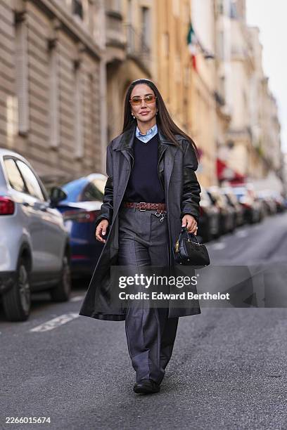 Tamara Kalinic wears dark brown hair, orange tinted sunglasses, a dark gray fabric and black leather bi material long coat from Miu Miu, a light blue...