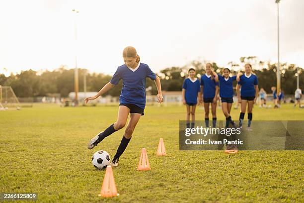 girls soccer team training on field dribbling ball around cones - club soccer stock pictures, royalty-free photos & images