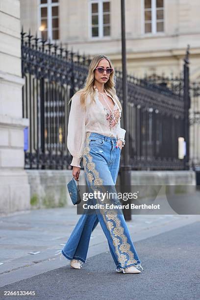 Guest wears pink cat eyes sunglasses, a white sheer V-neck long sleeve blouse, a pink floral embossed corset top, blue denim wide leg jeans with...