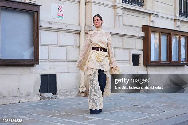 Guest wears dark brown hair in a bun, a cream lace high neck / long flared sleeves / belted tunic from Zimmermann, a black shiny leather belt, dark...