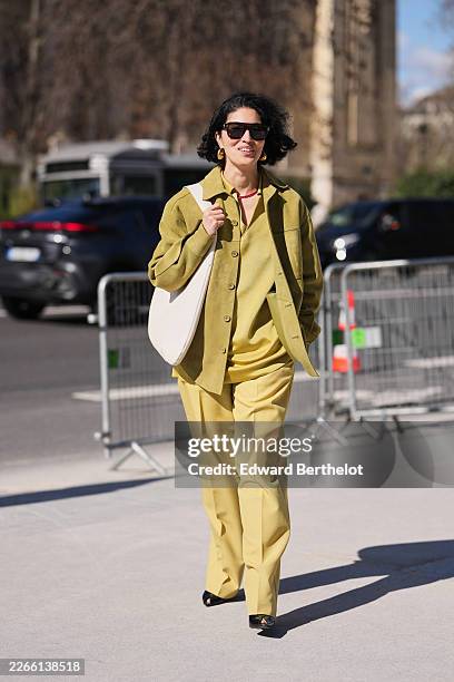 Guest wears black sunglasses, a green olive suede button front jacket, a yellow chartreuse knit polo shirt, matching yellow chartreuse wide leg...