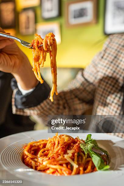 close-up of spaghetti pasta twirled on fork in casual restaurant dinner with tomato sauce - tomato pasta stock pictures, royalty-free photos & images