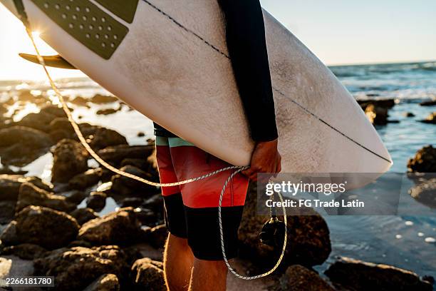 nahaufnahme eines jungen, der ein surfbrett am strand hält - surfbrett stock-fotos und bilder