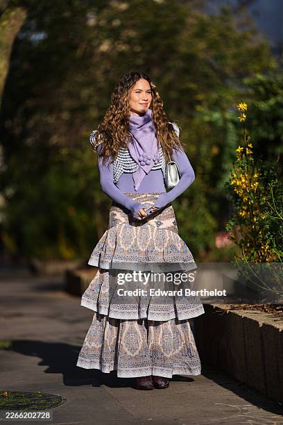 Guest wears brown wavy hair, a lavender knit turtleneck top, a gray knit cropped vest, a lilas wool scarf with embroidered pompom, a beige with...