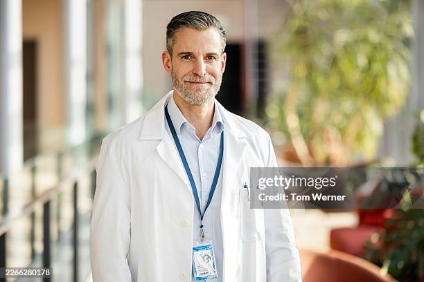 portrait of experienced mature male doctor standing in bright research facility corridor - lässig schicker stil stock-fotos und bilder