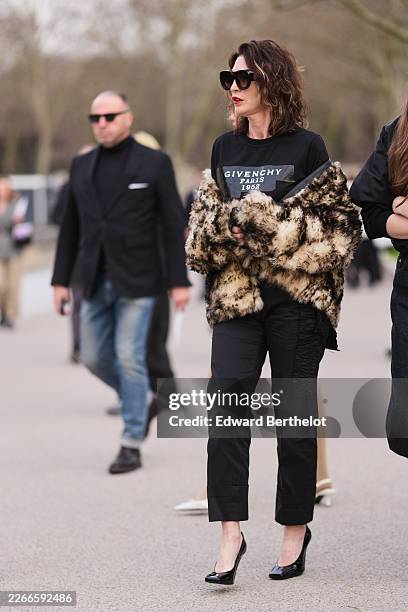 Guest wears dark wavy hair, black sunglasses, a beige faux fur leopard print coat, a black cotton logo sweatshirt from Givenchy, black straight leg...