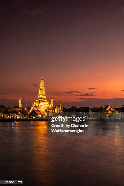 wat arun at sunset, bangkok. wide-angle scenic view of wat arun (temple of dawn) illuminated at sunset across the chao phraya river, bangkok, thailand. - golden hour stock pictures, royalty-free photos & images