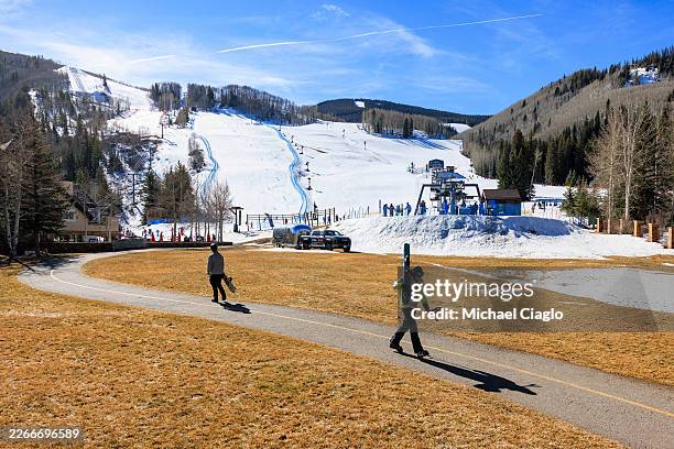 Skier and snowboarder walk through a grassy field to the chairlift at Vail Ski Resort as temperatures reach into the 50s on March 18, 2026 in Vail,...