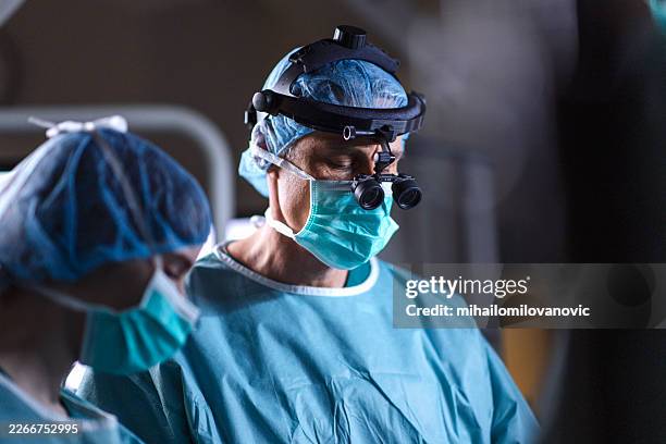 surgeon performing delicate operation in dim operating room - covid secure stock pictures, royalty-free photos & images