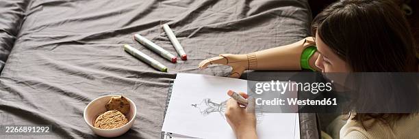 girl with prosthesis drawing a sketch on a bed in a creative setting - amputee stock illustrations