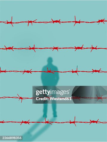 Shadow of a prisoner behind red barbed wire symbolizing restriction Shadow of a prisoner behind red barbed wire symbolizing restriction