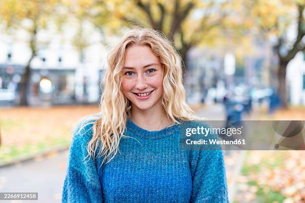 happy woman with blonde curly hair smiling outdoors in autumn park - platinum stock pictures, royalty-free photos & images