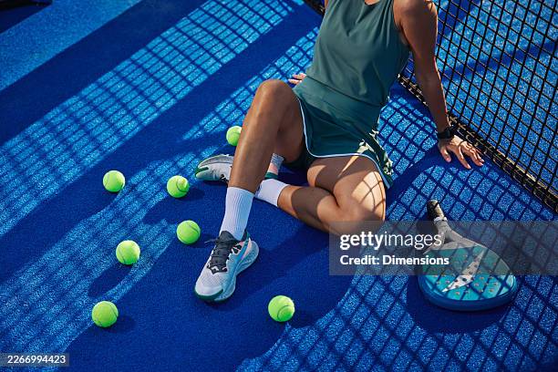 donna che si rilassa su un campo da padel blu circondata da palle e racchette dopo una partita informale - accessorio personale foto e immagini stock