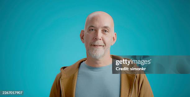 portrait d’atelier d’un homme caucasien mature souriant doucement contre un mur bleu vif - complètement chauve photos et images de collection