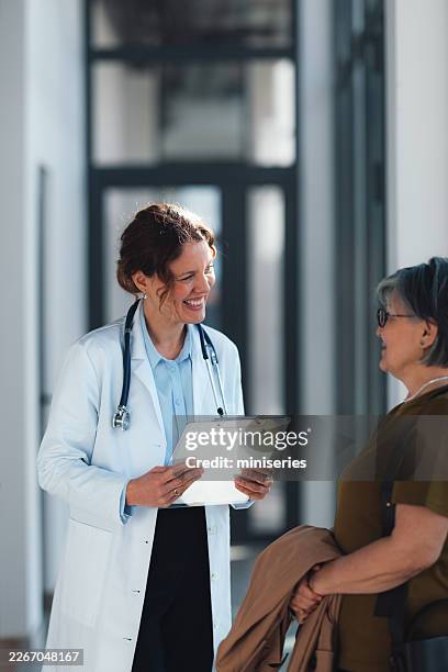 smiling female doctor consulting senior woman patient in hospital corridor building trust in healthcare - kindness stock pictures, royalty-free photos & images