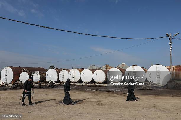 People walking in front of oil barrels at a market for fuel oil and automotive fuel on March 17, 2026 in Erbil, Iraq. Recent drone attacks in the...