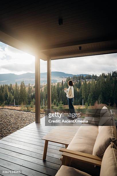 young woman enjoys hot beverage on outdoor porch - porch stock pictures, royalty-free photos & images