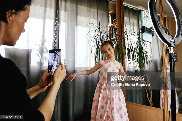 8 years old girl and her mother playing at home, using smartphone with ring light for live streaming - vlogger stockfoto's en -beelden