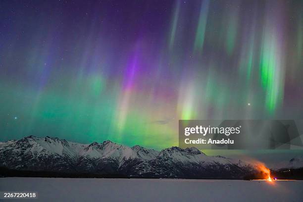 Northern Lights illuminate the night sky with vivid purple and green hues above a distant cityscape following a strong solar storm coinciding with...