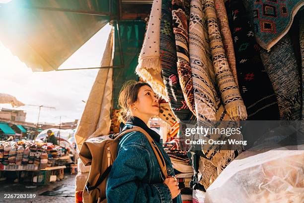 young asian woman admiring a beautifully woven moroccan rug in the market - solo travel stock pictures, royalty-free photos & images