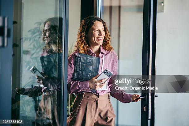empresaria feliz llegando al edificio de oficinas con tablet y teléfono - llegada fotografías e imágenes de stock