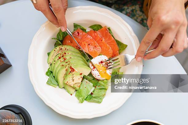 close-up overhead view of a woman sitting at a garden table in summer eating a salmon, avocado, and poached egg salad - ketogenic diet stock pictures, royalty-free photos & images