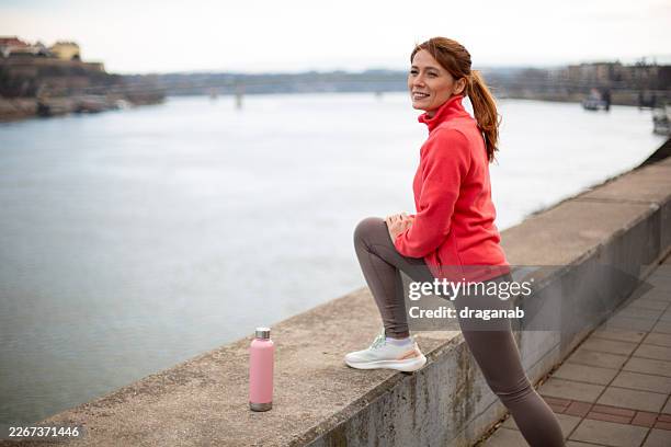 woman stretching outdoors by river preparing for run - embankment stock pictures, royalty-free photos & images