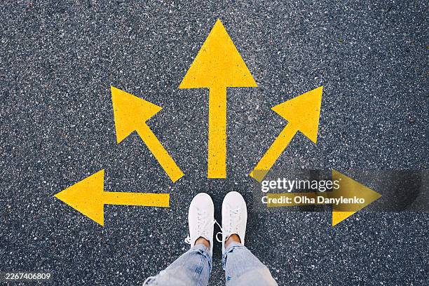top view of a person standing on asphalt with yellow arrows pointing in different directions. - entscheidung stock-fotos und bilder