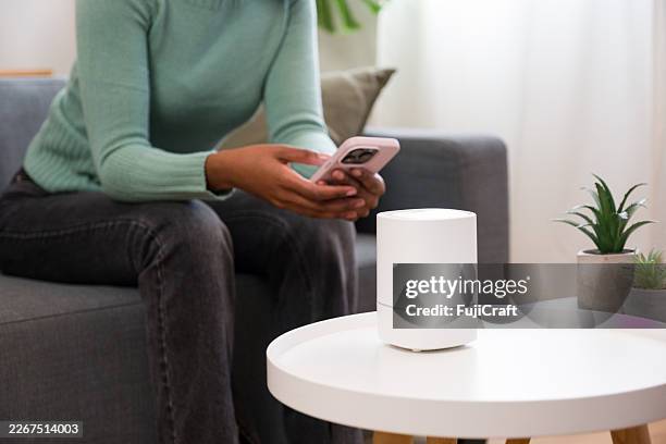 person controlling smart speaker with smartphone in living room - router stock pictures, royalty-free photos & images