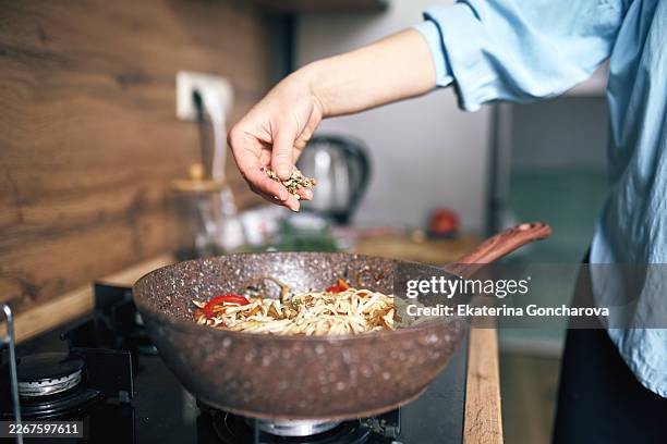 woman cooking noodles in pan on gas stove in modern home kitchen, sprinkling seasoning - comfort food stock pictures, royalty-free photos & images