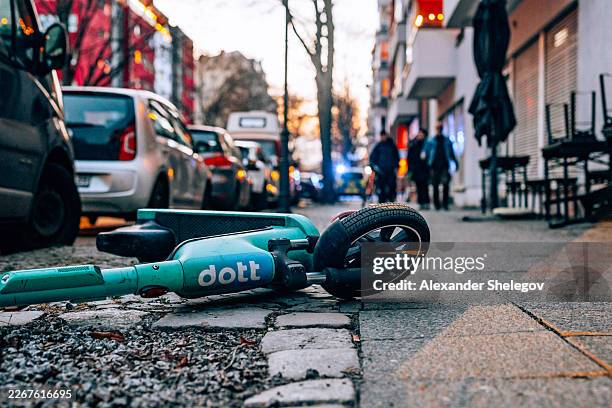 dott electric scooter lying on berlin sidewalk with police lights blurred in background - elektrische step stockfoto's en -beelden