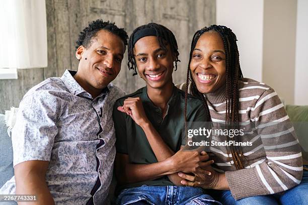 black family smiling, relaxing together on a sofa at home. - african american ethnicity stock pictures, royalty-free photos & images