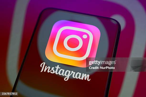 The Instagram logo appears on the screen of a smartphone placed on a reflective surface onto which another icon of the application is projected, in...