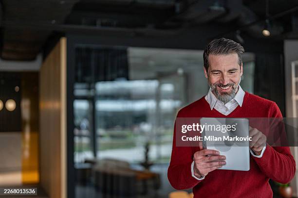 man smiling while using digital tablet in modern office - red tablets stock pictures, royalty-free photos & images