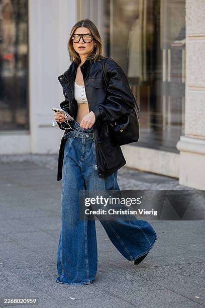 Sophia Geiss wears Apple headphone cables black oversized leather jacket Meotine, sunglasses Prada, flared denim jeans & cropped top Closed, shoes...