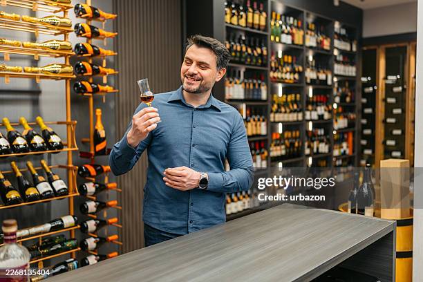 mid-adult man tasting whiskey in a liquor store - whiskey tasting stock pictures, royalty-free photos & images
