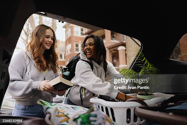 two happy young women students loading belongings into car trunk for college move - student accommodation stock pictures, royalty-free photos & images