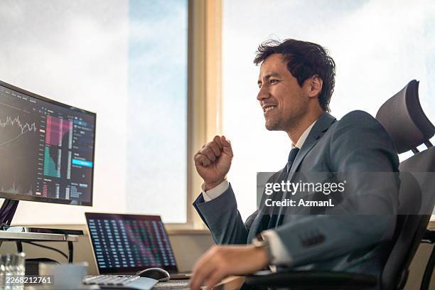 successful asian trader celebrating at modern trading desk with market charts - stock market trader stock pictures, royalty-free photos & images
