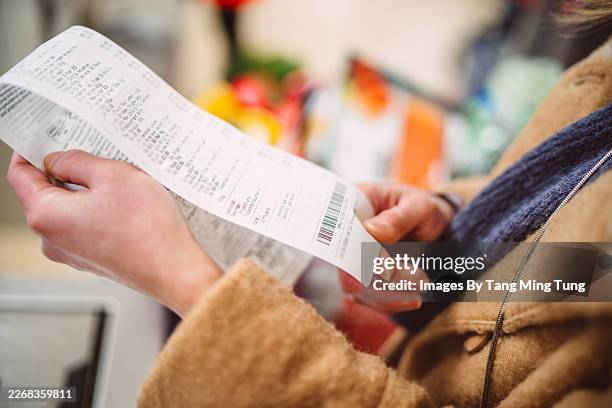 woman reviewing shopping receipt after grocery purchase - beleg stock-fotos und bilder