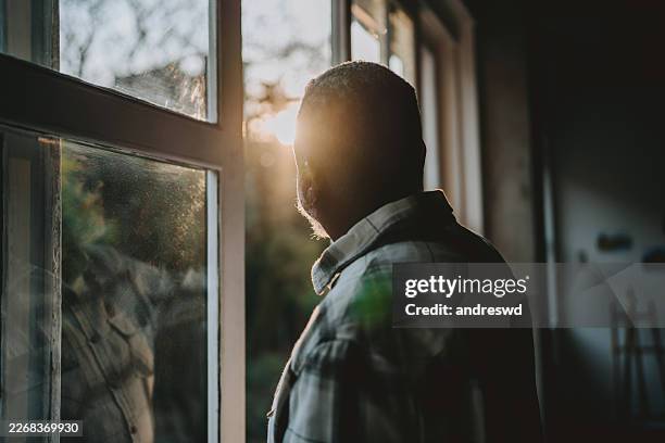 portrait of an elderly man looking out the window, alone - depressie stockfoto's en -beelden