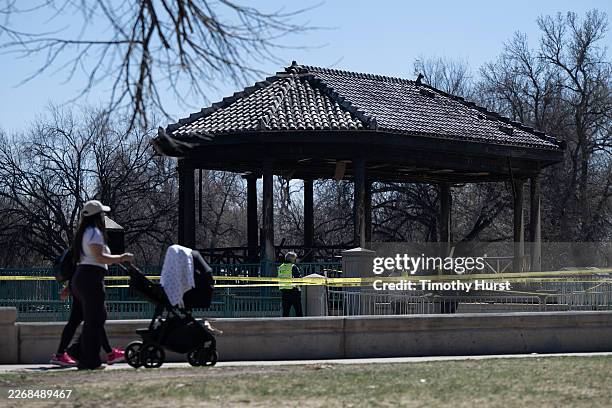 Two people push a stroller past the burned remains of the bandstand at City Park after an overnight fire on Thursday, March 26 at City Park in...