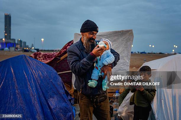 Displaced man feeds his baby with a bottle in front of a family tent in an unofficial camp, erected along Beirut's seafront area on April 1, 2026....
