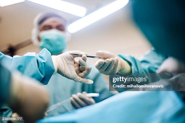 équipe chirurgicale passant un scalpel pendant l’opération dans la salle d’opération - scalpel photos et images de collection