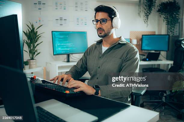 male programmer wearing headphones while coding in modern office - web programmer stock pictures, royalty-free photos & images