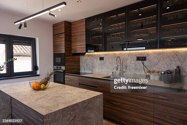 modern walnut kitchen with marble island, integrated appliances and ambient under-cabinet lighting - soapstone stock pictures, royalty-free photos & images