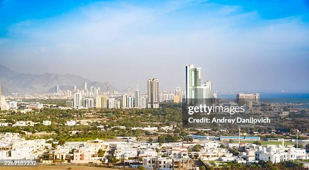 panoramic high angle view of fujairah city skyline with modern skyscrapers and mountains under blue sky in united arab emirates - high section stock pictures, royalty-free photos & images