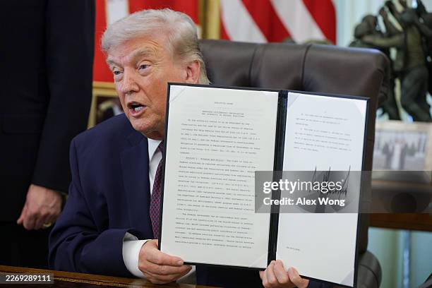 President Donald Trump holds up an executive order to limit mail-in voting in the Oval Office of the White House on March 31, 2026 in Washington, DC....